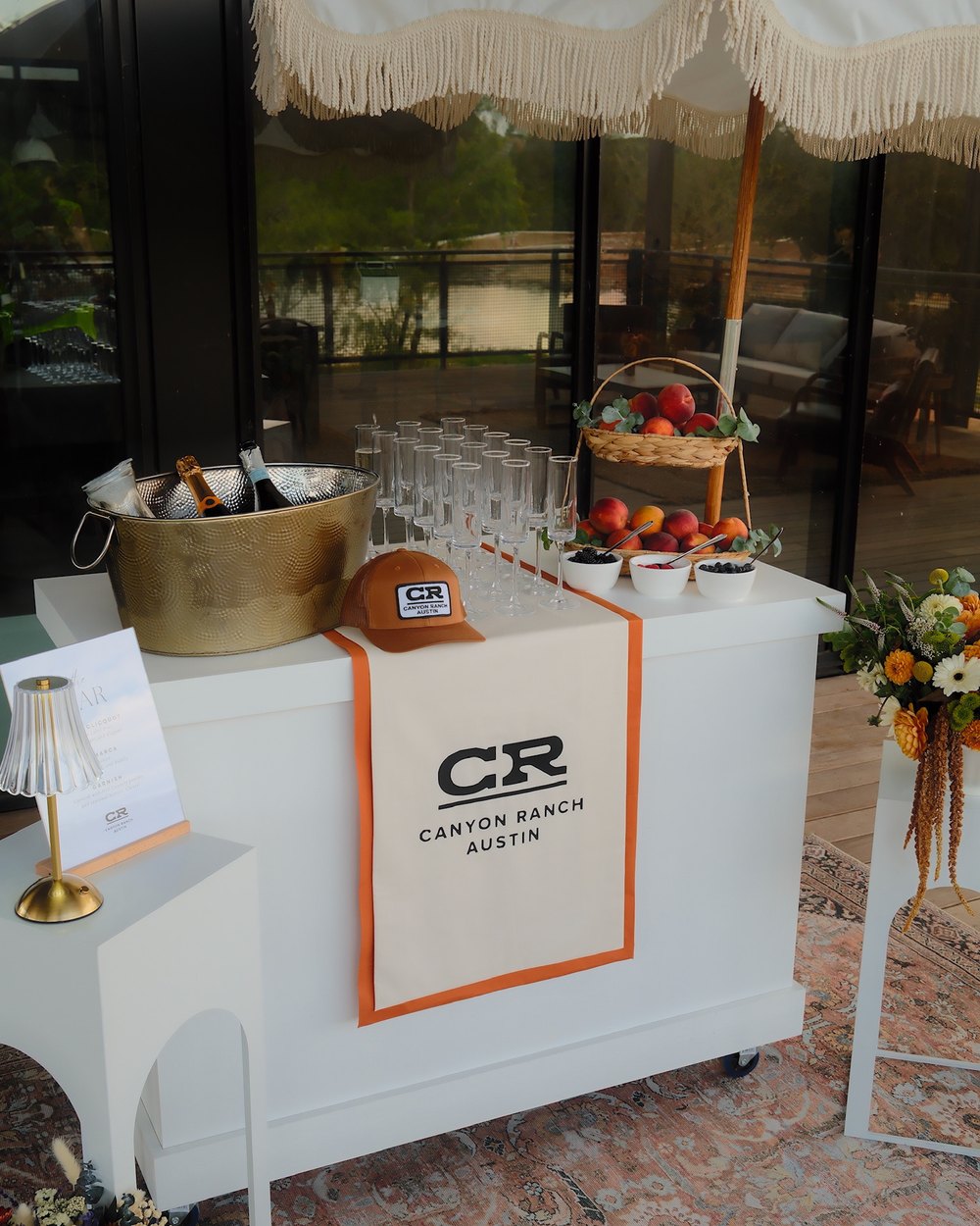 Branded champagne bar cart with a gold ice bucket, flutes, and fresh peaches at a Canyon Ranch Austin event