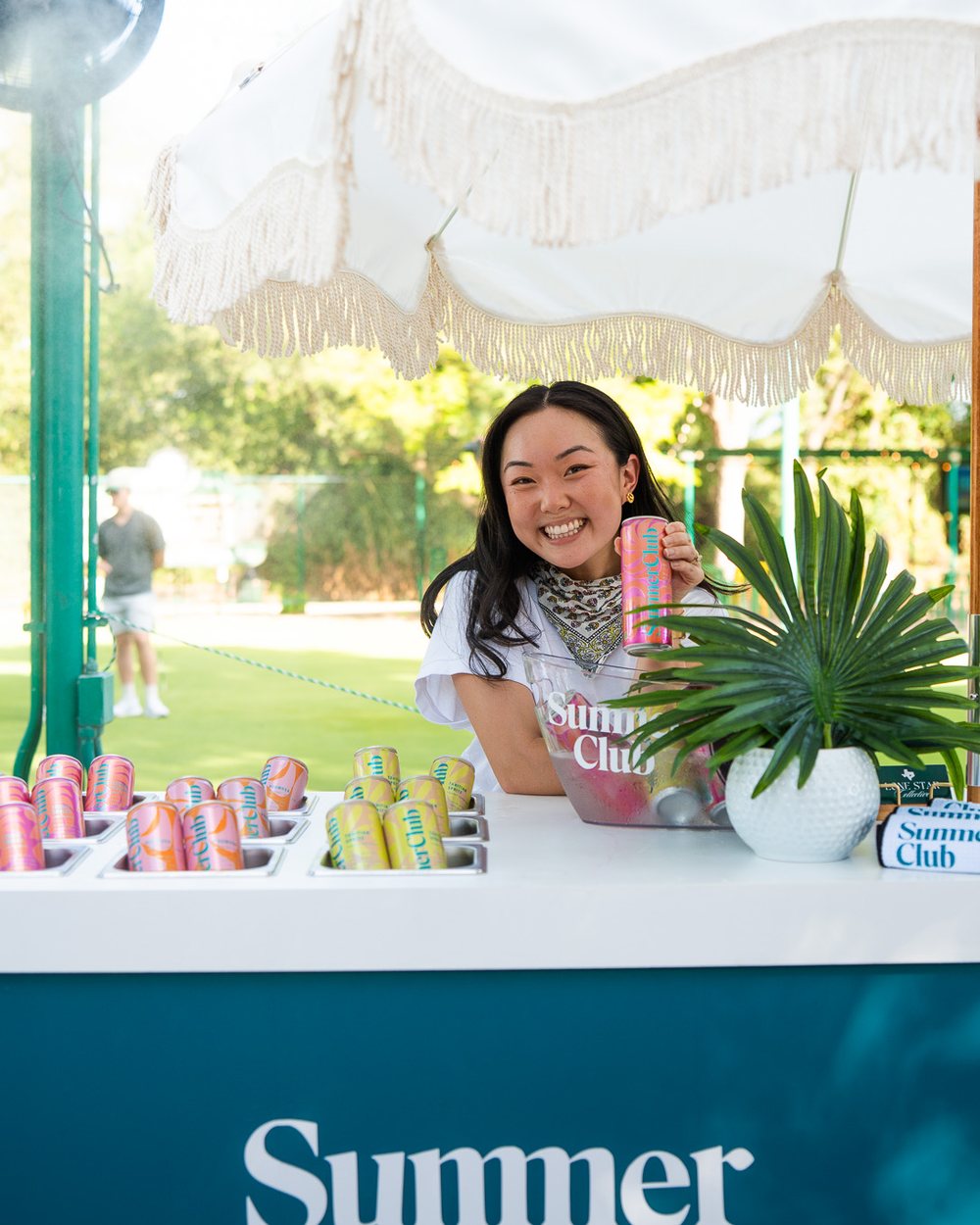 Branded beverage cart with cans and a fringed umbrella on an Austin golf course
